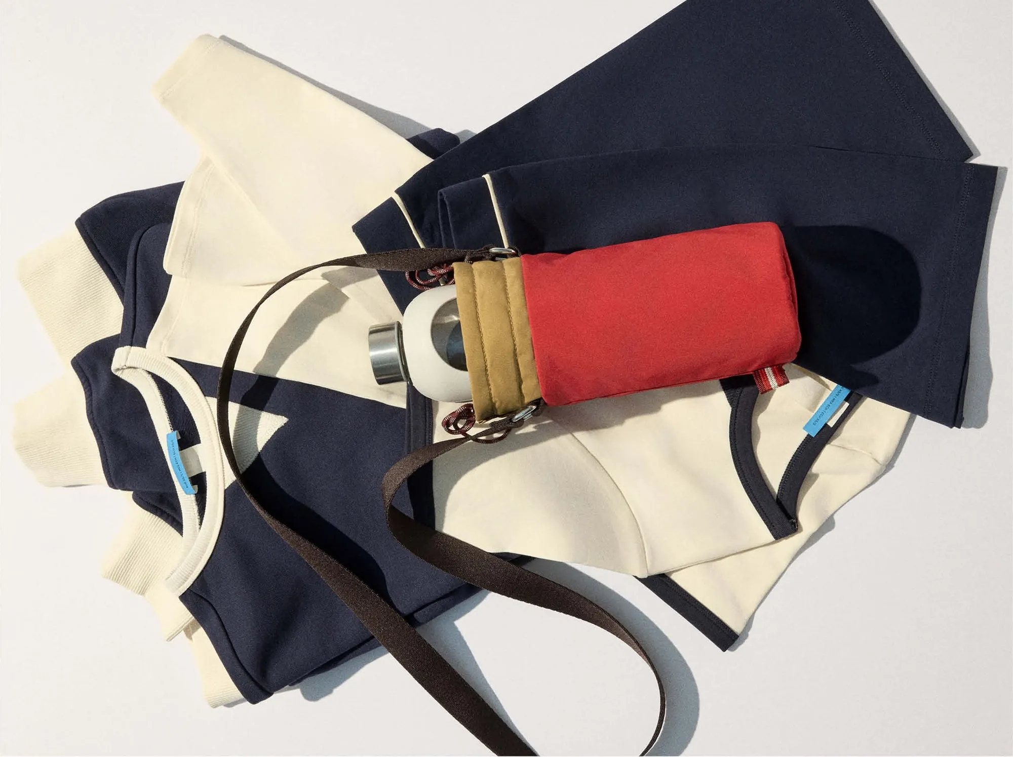 Flat lay: cream sweatshirt, navy shorts, the red bottle holder and its glass bottle
