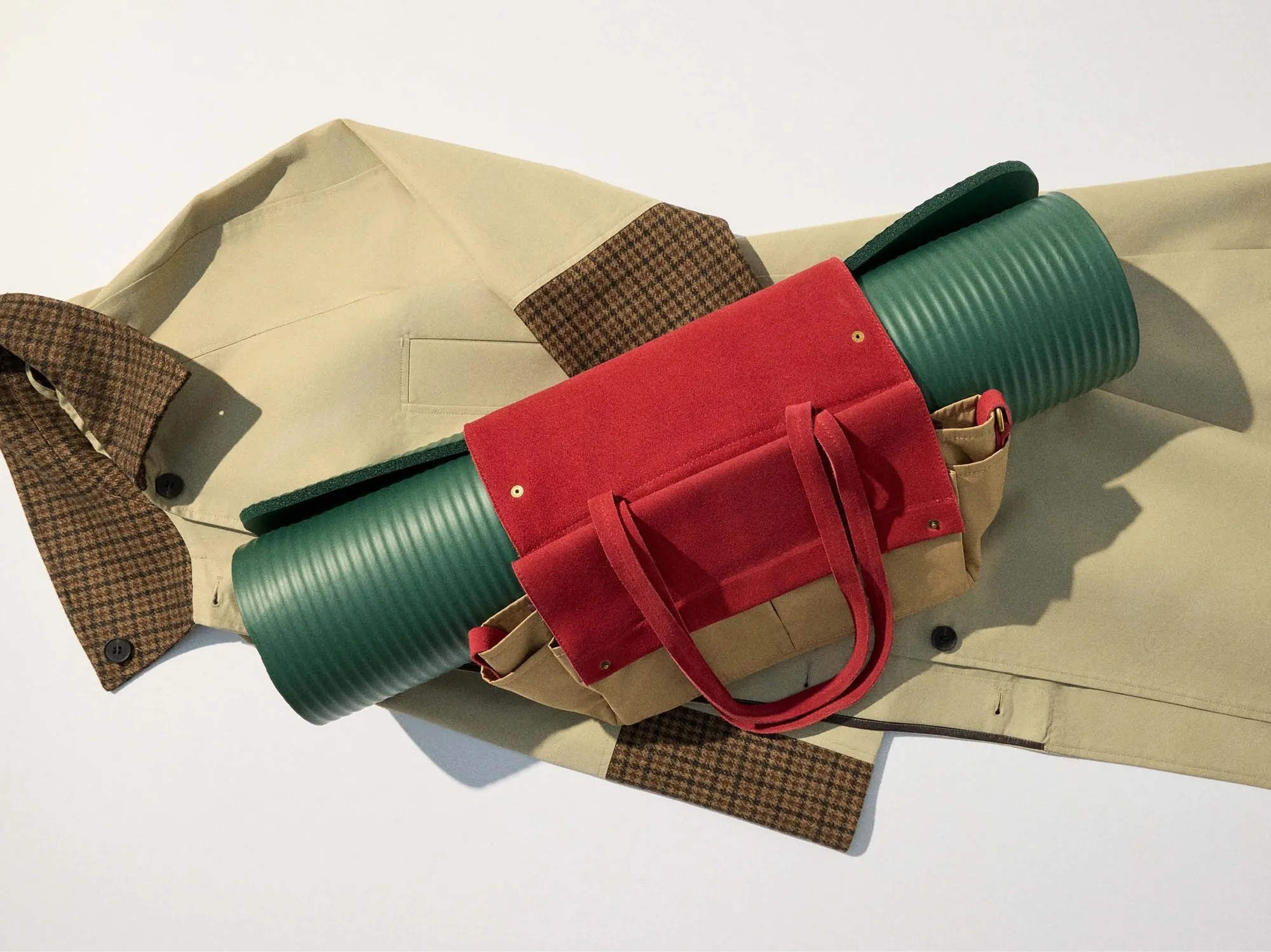 The trench coat laid flat with a green mat rolled in the red mat bag
