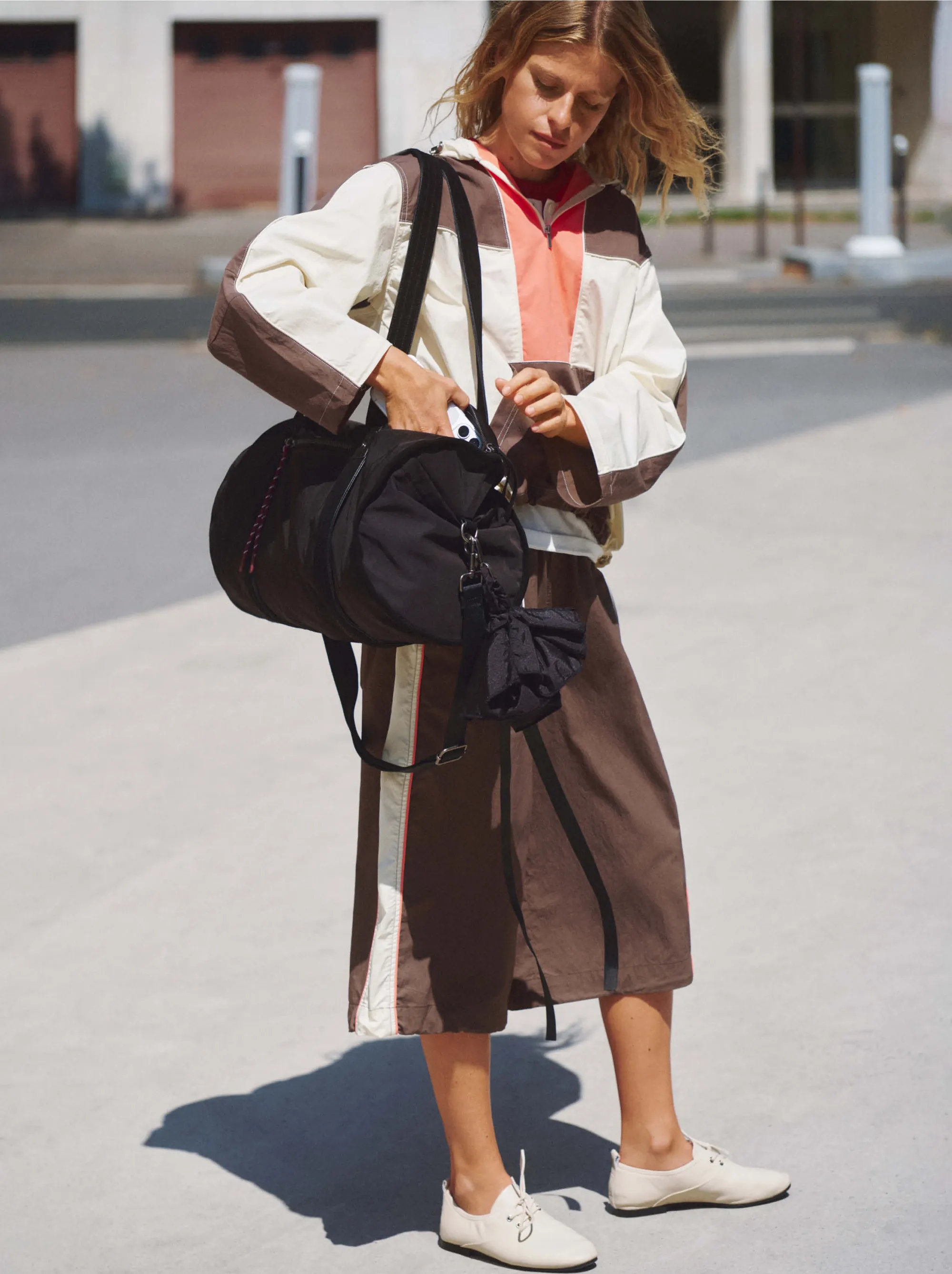 Crossing a Paris street in the colour-block windbreaker and brown Bermuda shorts, the black sports bag on the shoulder