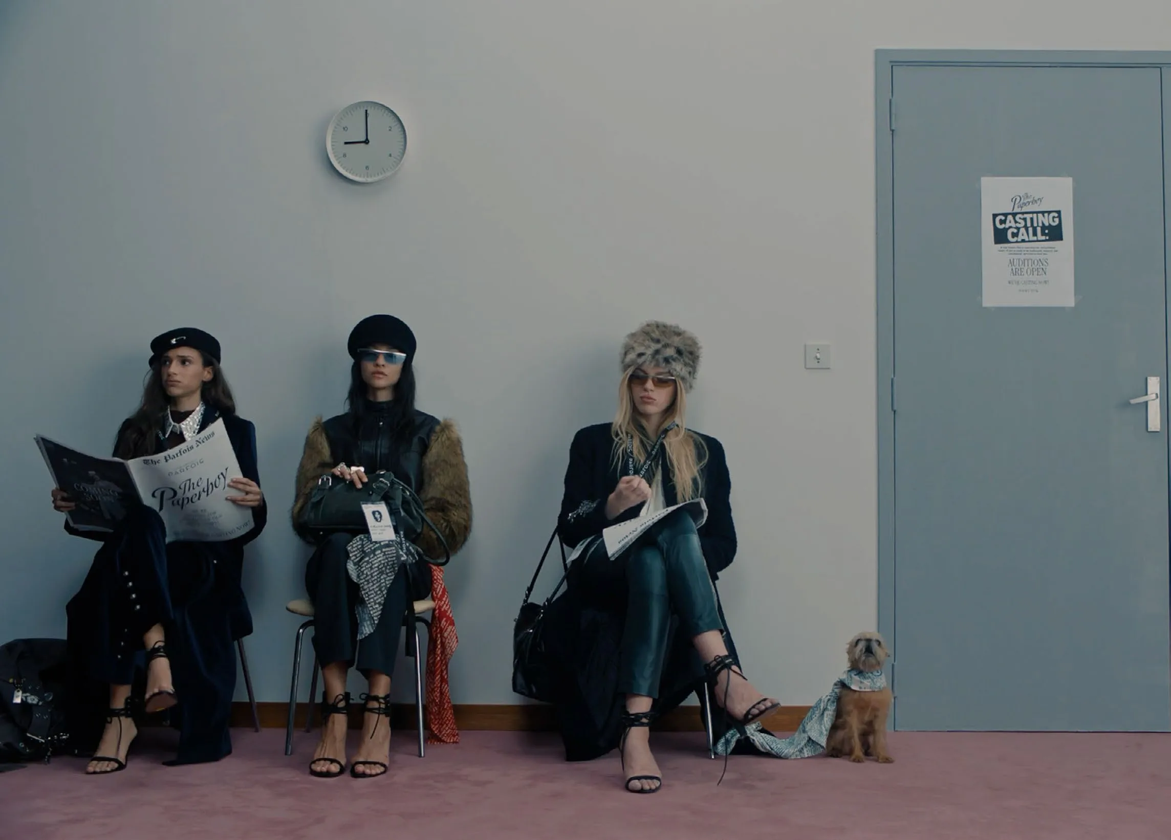 Three candidates seated in the waiting room under a wall clock, a small dog beside them