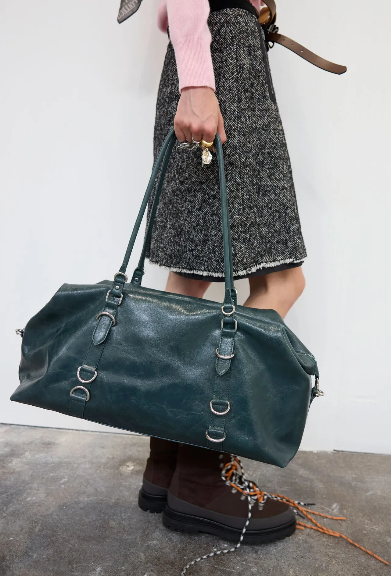 Deep green leather holdall carried past a tweed skirt