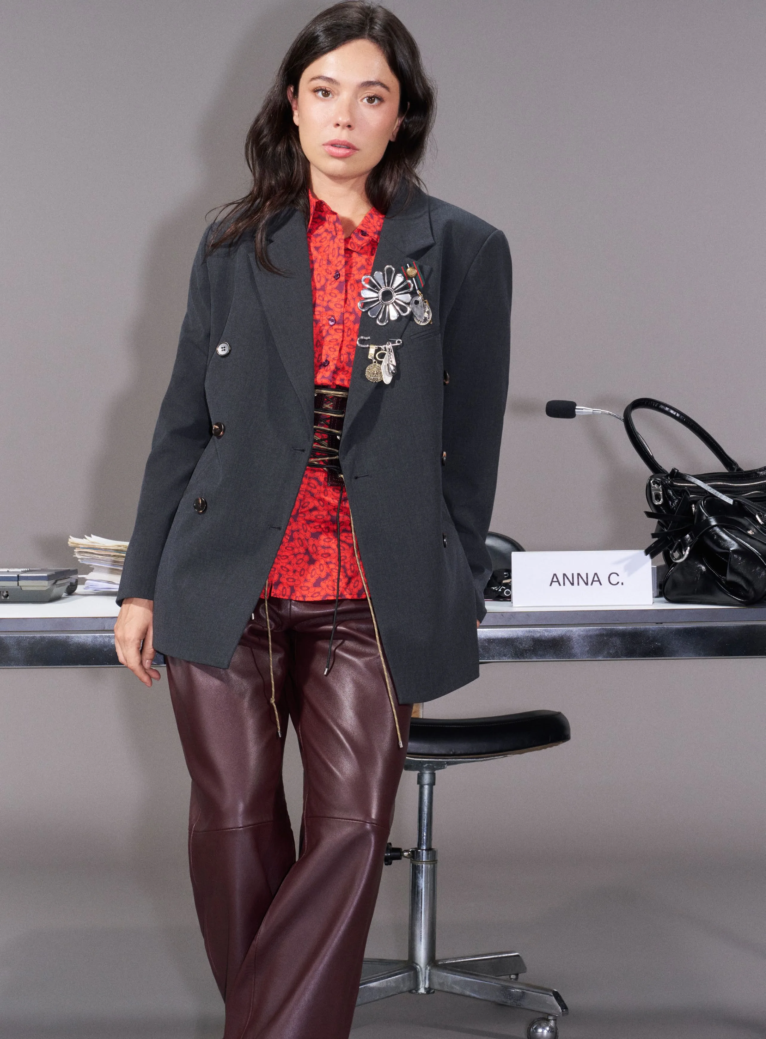 Anna C. seated at the casting table in a grey blazer and leather trousers