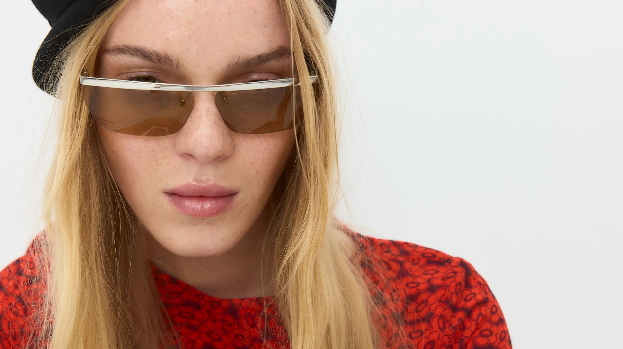 Close crop of narrow sunglasses over a printed red dress