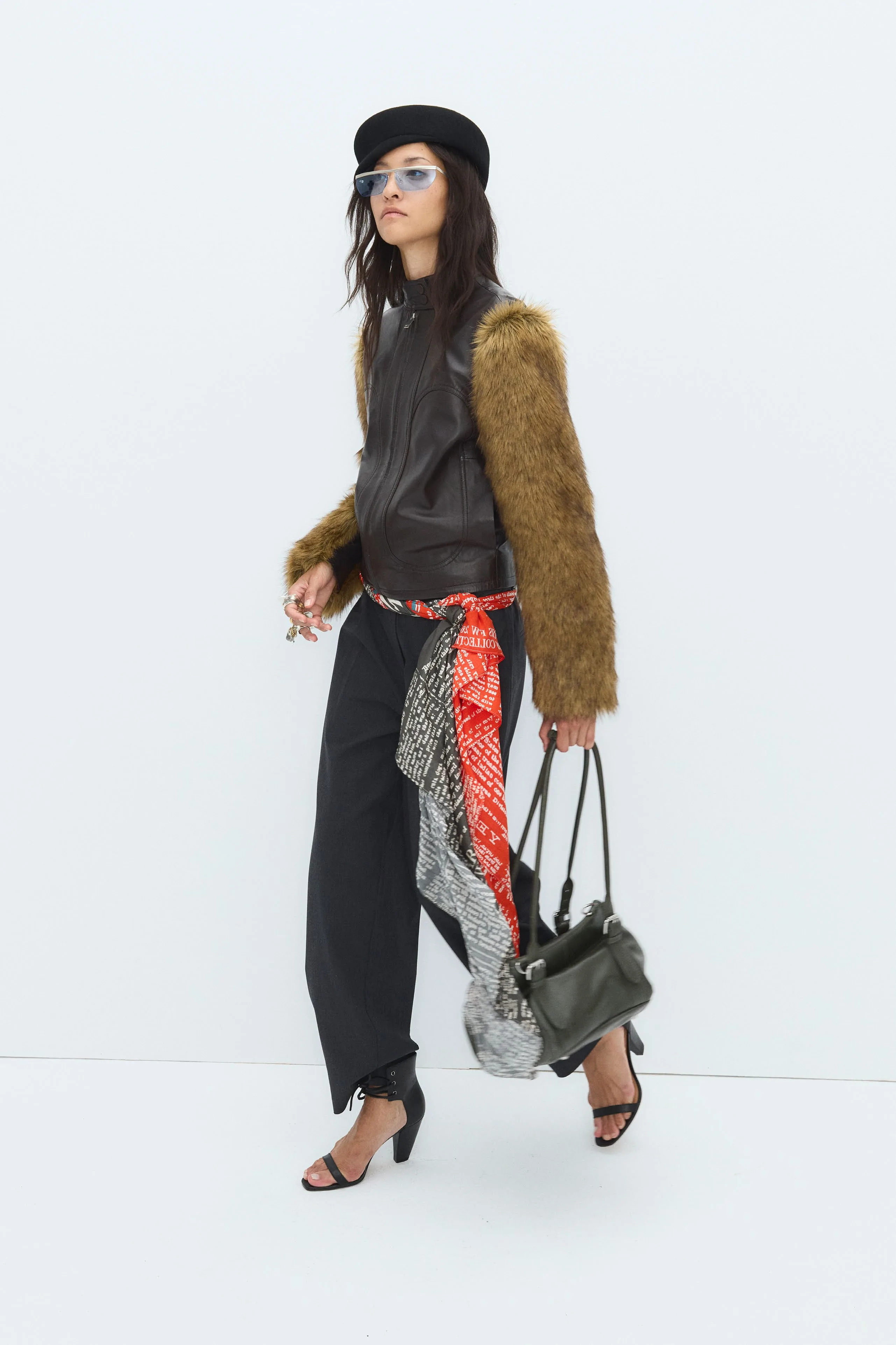 Colin in a leather vest with fur sleeves, sandals and a slouch bag