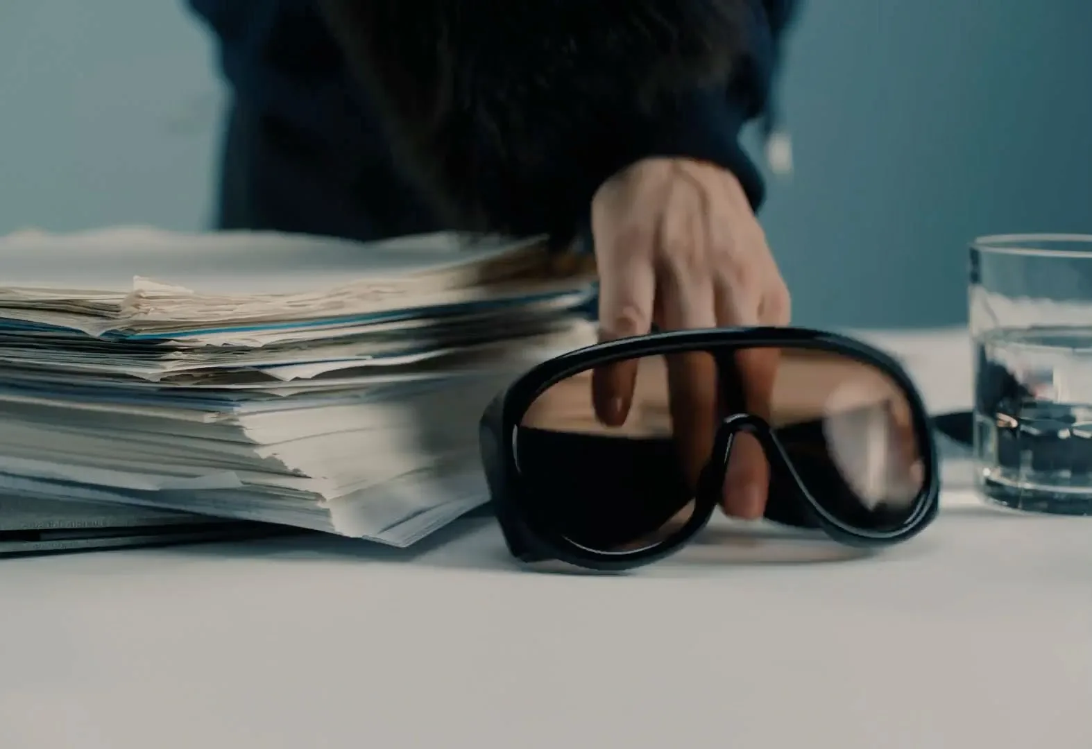 A hand rests on the stack of newspapers beside dark glasses